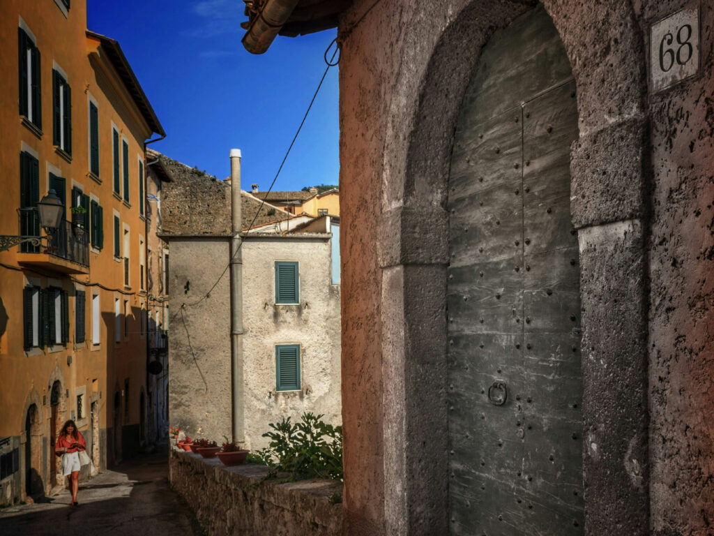 Gade i Arpino med bygninger, planter og en gående kvinde på billedet.