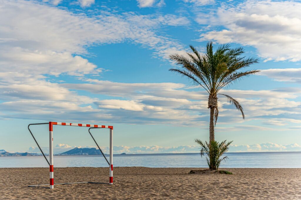 Strandfodboldmål og ensom palme med udsigt til hav og fjerne bjerge.