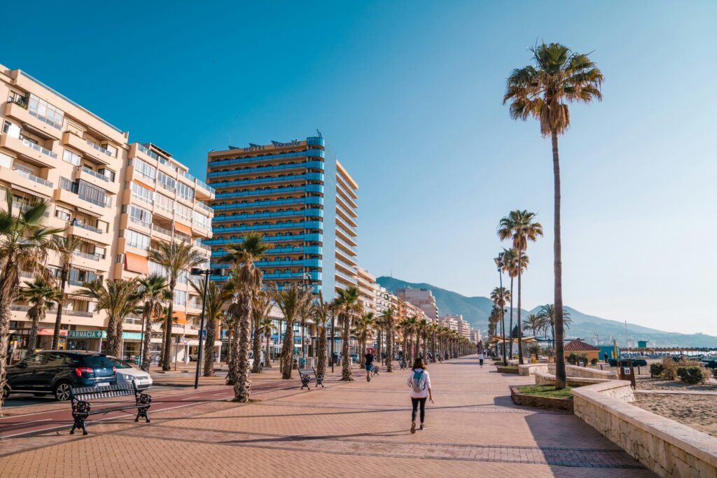 Fuengirolas solbeskinnede strandpromenade med palmer, hoteller og udsigt til bjergene.